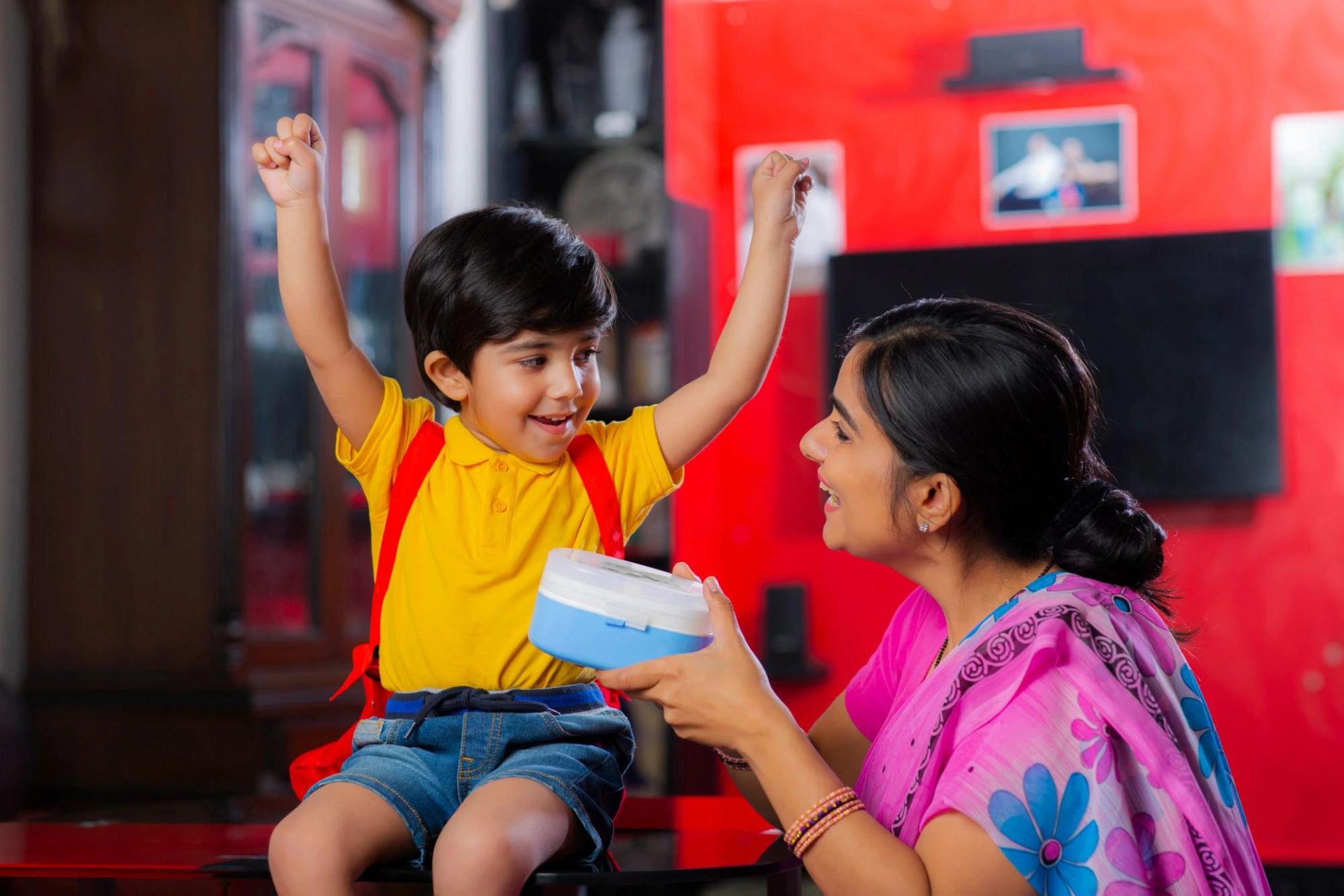 Excited boy receiving his school lunchbox from his mother